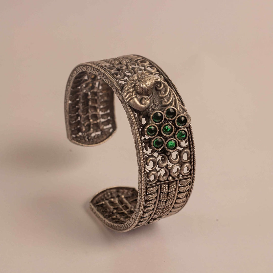 Decorative silver bracelet with green gemstones on a beige background
