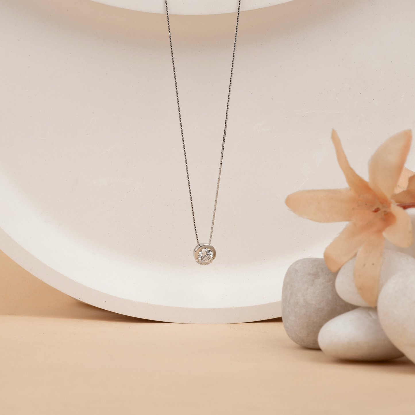 Delicate silver necklace with a round pendant on a neutral background