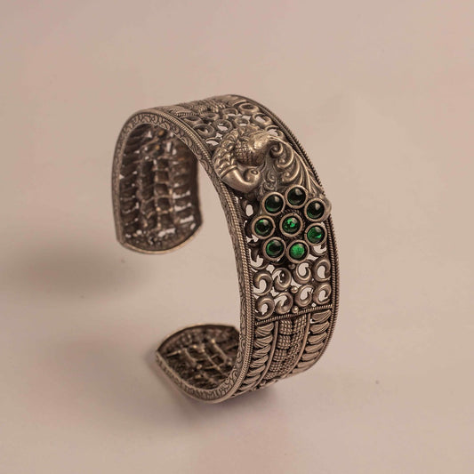 Decorative silver bracelet with green gemstones on a beige background
