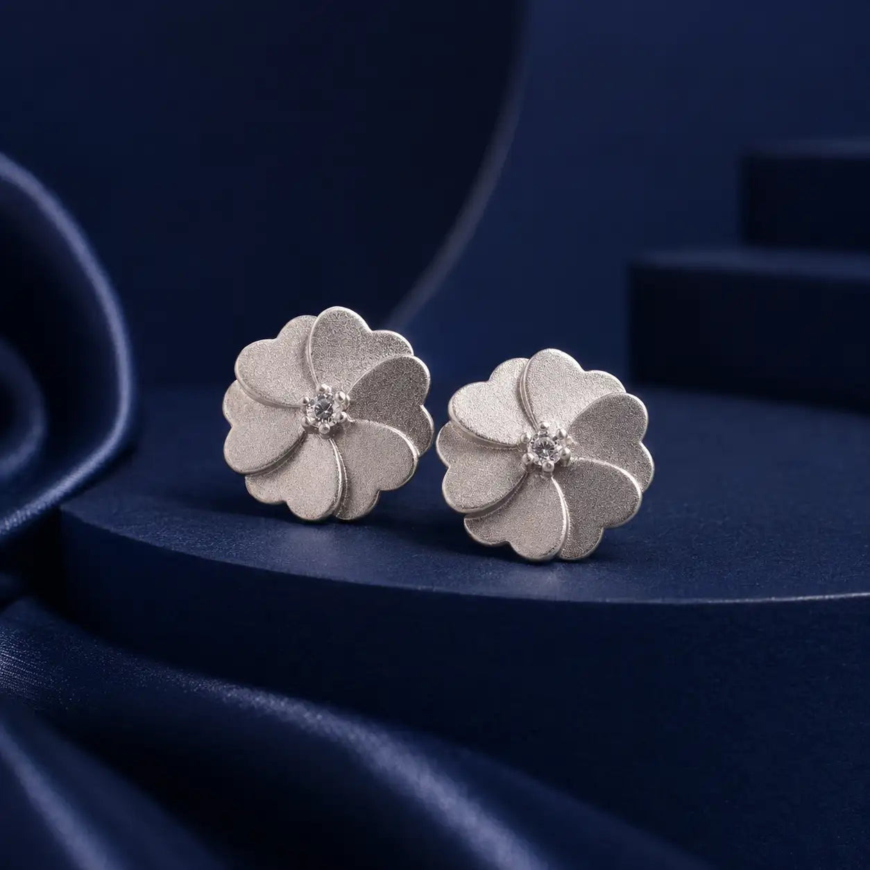 Silver flower-shaped stud earrings with a textured surface and tiny clear gemstones at the center.